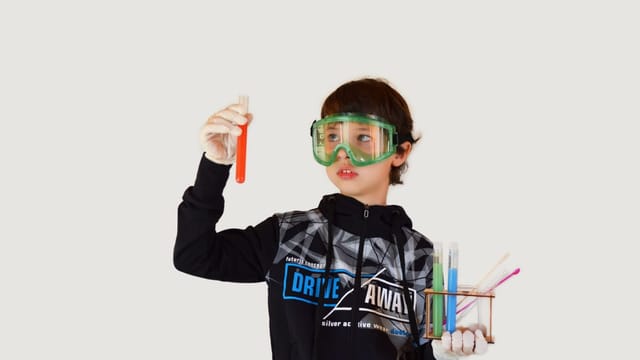 Young student in a lab coat and safety goggles holding a test tube