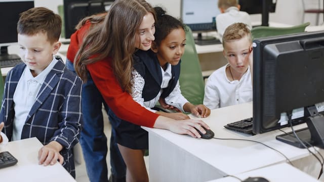 A teacher and students in front of a computer in a classroom